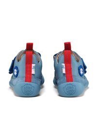 Scarpe per bambini blu con accenti rossi, in morbida pelle, con cinturini in Velcro e un logo rotondo. Suola in gomma testurizzata con marchio.
