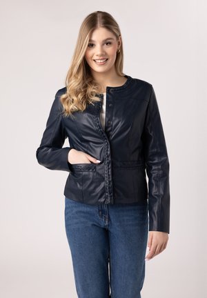 Giacca di pelle blu navy con un design fitted, chiusura a bottone automatico e dettagli intrecciati sul davanti e sulle tasche. Indossata sopra una maglia leggera.