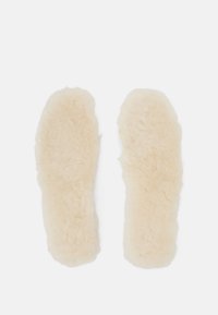 Saueskinnsåler i en lys beige farge med en myk, fluffy tekstur, formet for å passe komfortabelt inne i fottøy.