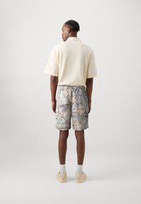 Beige polo shirt with a textured pattern, paired with camo print shorts in grey and green. Footwear is light-colored with raised soles.