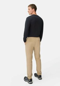 Langärmliges schwarzes Shirt kombiniert mit beigen Hosen. Die Hose hat Gesäßtaschen und einen geraden Schnitt. Schwarze Schuhe runden das Outfit ab.