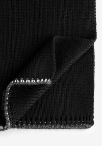 Gefalteter schwarzer Strickstoff mit weißen gestickten Details entlang der Kanten auf einem weißen Hintergrund.