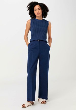 Haut sans manches en tricot marine avec un motif texturé, associé à un pantalon large marine et des sandales claires avec une lanière tissée.
