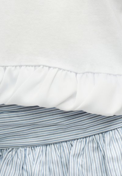Tissu blanc avec un volant froncé au-dessus de couches de tissu froncé à rayures verticales bleues et blanches.