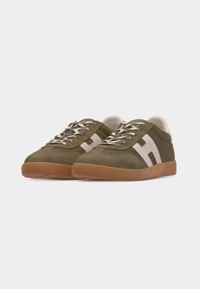 Paire de baskets en daim vert olive avec un logo "H" blanc sur les côtés, des lacets à motifs et des semelles en gomme, légèrement inclinées vers la droite.
