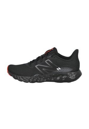 Zapatilla deportiva negra con parte superior de malla transpirable, cuello acolchado y suela negra texturizada con acentos rojos. Diseño de logo notable en gris.