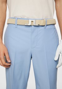 Beige vävt bälte med silverfärgad metallspänne, kombinerat med ljusblå byxor i en slät tygkvalitet och skräddarpassform.