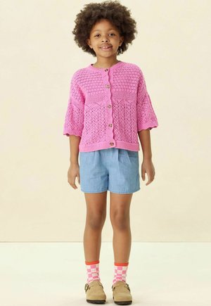 Roze gebreide cardigan met korte mouwen, met een getextureerd patroon en knopen. Gecombineerd met denim shorts en kleurrijke gestreepte sokken.