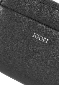 Černá kožená peněženka s texturovaným povrchem a stříbrným logem „JOOP!“. Vyznačuje se čistými liniemi a štíhlým designem.