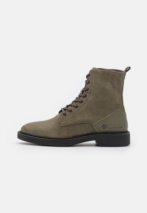Olive green ankle boots made of textured suede, featuring a round toe, lace-up front, and a sturdy black rubber sole. G-Star Raw branding visible.