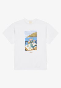 T-shirt en coton blanc avec un imprimé graphique d'une table avec des fleurs et des tasses, sur fond de paysage côtier.