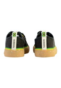 Scarpe in tessuto nero con suola in gomma. Accenti verde e giallo lungo il lato e il tallone, con un'etichetta marchiata che presenta una bandiera brasiliana.