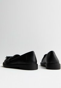 Mocassini in pelle nera con tacco basso, dotati di un dettaglio decorativo a frange sulla parte anteriore e finitura liscia. Design minimalista, punta arrotondata.