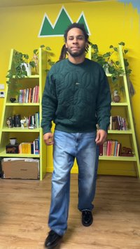 Grøn quiltet sweatshirt med rund halsudskæring, kombineret med lyseblå løse jeans og sorte sko, går i et lyst gult rum.