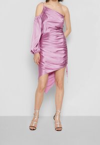 Růžové saténové šaty na jedno rameno se skládáním, s dlouhým nařaseným rukávem a asymetrickým lemem. Vzhled dokončují černé sandály na tenkých páscích.