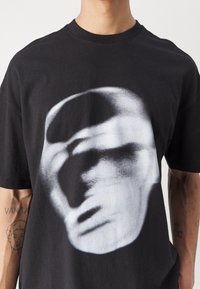 Black cotton t-shirt featuring a large, abstract white graphic design resembling a face, with a crew neckline and short sleeves.