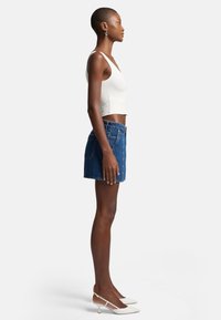 Top court blanc, jupe en denim et chaussures à talons blanches. Présente un design ajusté, une texture en denim bleu, et une jupe de longueur mi-cuisse.