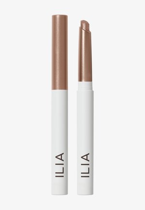 To ILIA shimmer øjenskygge-sticks med hvide baser og metallisk bronze låg, den ene lukket og den anden åben, hvilket viser den skrå produktspids.
