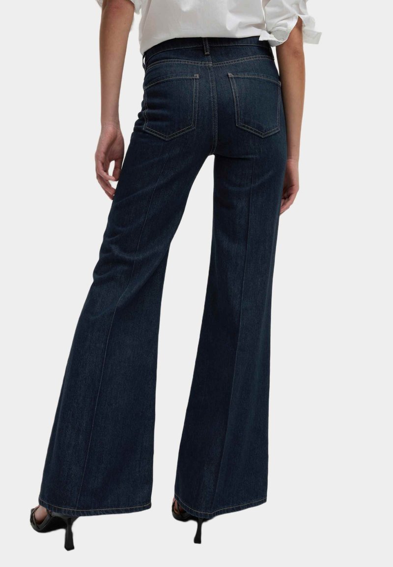 Jeans de mezclilla de campana de color azul oscuro, con una alta cintura, bolsillos traseros y un acabado limpio sin adornos visibles.