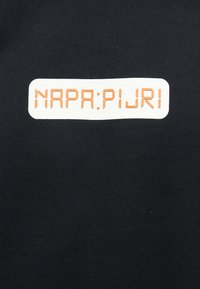 Μαύρο ύφασμα με ένα λευκό ορθογώνιο έμπλαστρο που φέρει το κείμενο "NAPA:PIJRI" σε πορτοκαλί ψηφιακό στυλ γραμματοσειράς.