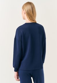 Felpa blu navy con vestibilità ampia, polsini a costine e collo rotondo. Tessuto morbido, con design senza cuciture e maniche scese.