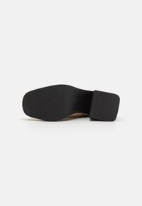 Black shoe sole with textured grip pattern, square shape, and a thick heel. Material appears to be rubber. Neutral color and minimal design.