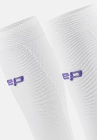 White athletic socks featuring a ribbed texture and purple logo. The design includes an elastic cuff for fit and comfort.