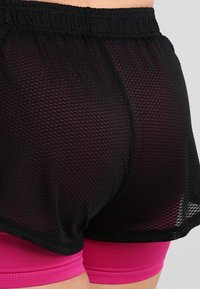 Bermudas atléticas de malla negras superpuestas sobre pantalones cortos fucsias ajustados, con una cinturilla elástica y un diseño ligero y transpirable.