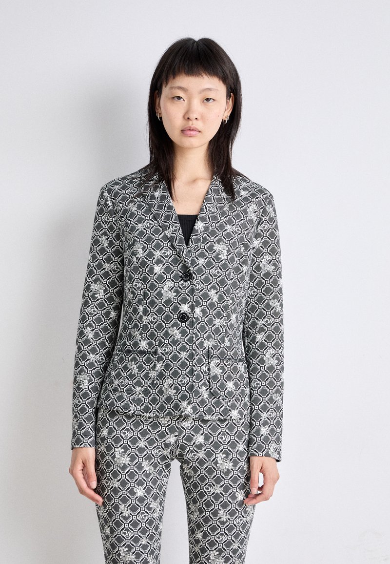 Grau gemusterter Blazer mit hexagonalem und floralem Druck, ausgestattet mit einem Reverskragen, zwei Knöpfen und passenden, taillierten Hosen. Strukturierter Stoff.