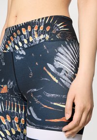 Hoogwaisted leggings in een kleurrijk, abstract patroon met tinten zwart, oranje en wit, gemaakt van een gladde, rekbare stof en met een contrasterende tailleband.
