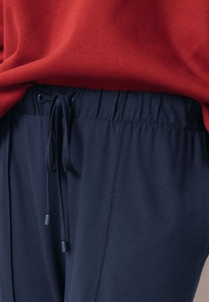 Pantalones azul marino con cintura elástica y cordón atado al frente, combinados con un top rojo metido por dentro.