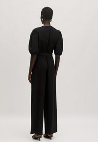 Zwarte jumpsuit met opgeblazen mouwen, een taille die cinched is, wijde pijpen en een gladde stof, met minimale stiksels en een schone esthetiek.