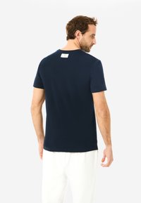 Marineblaue T-Shirt aus glattem Stoff, mit kurzen Ärmeln und Rundhalsausschnitt. Beinhaltet ein kleines Etikett, das am hinteren Halsansatz angenäht ist.