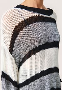 Pulover supradimensionat cu dungi alb-negru, realizat dintr-un tricot lejer. Dispune de un gât larg în stil boat neck și dungi de grosimi variate într-o textură translucidă.