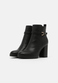 Botas tobilleras de cuero negro con un acabado suave, con una correa de hebilla lateral y un tacón ancho. Panel texturizado a los lados.
