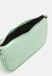 Mała torebka w kolorze miętowym z teksturą krokodylej skóry, częściowo otwarty srebrny zamek i czarne wykończenie wnętrza na białym tle.