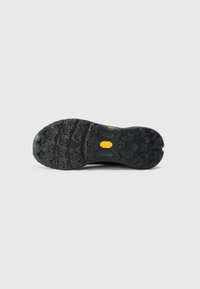Semelle de chaussure d'extérieur noire en caoutchouc texturé, avec de profonds crampons et un logo visible. Construction durable pour traction et stabilité.