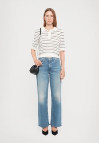 Wit gestreepte polo met korte mouwen, lichtblauwe flared jeans, zwarte handtas en zwarte hoge hakken. Zachte katoen en denim texturen.