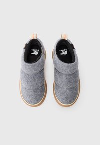 Par de zapatos de felpa gris sin cordones con suelas de goma color marrón claro y lengüetas para tirar, exhibidos sobre un fondo blanco.
