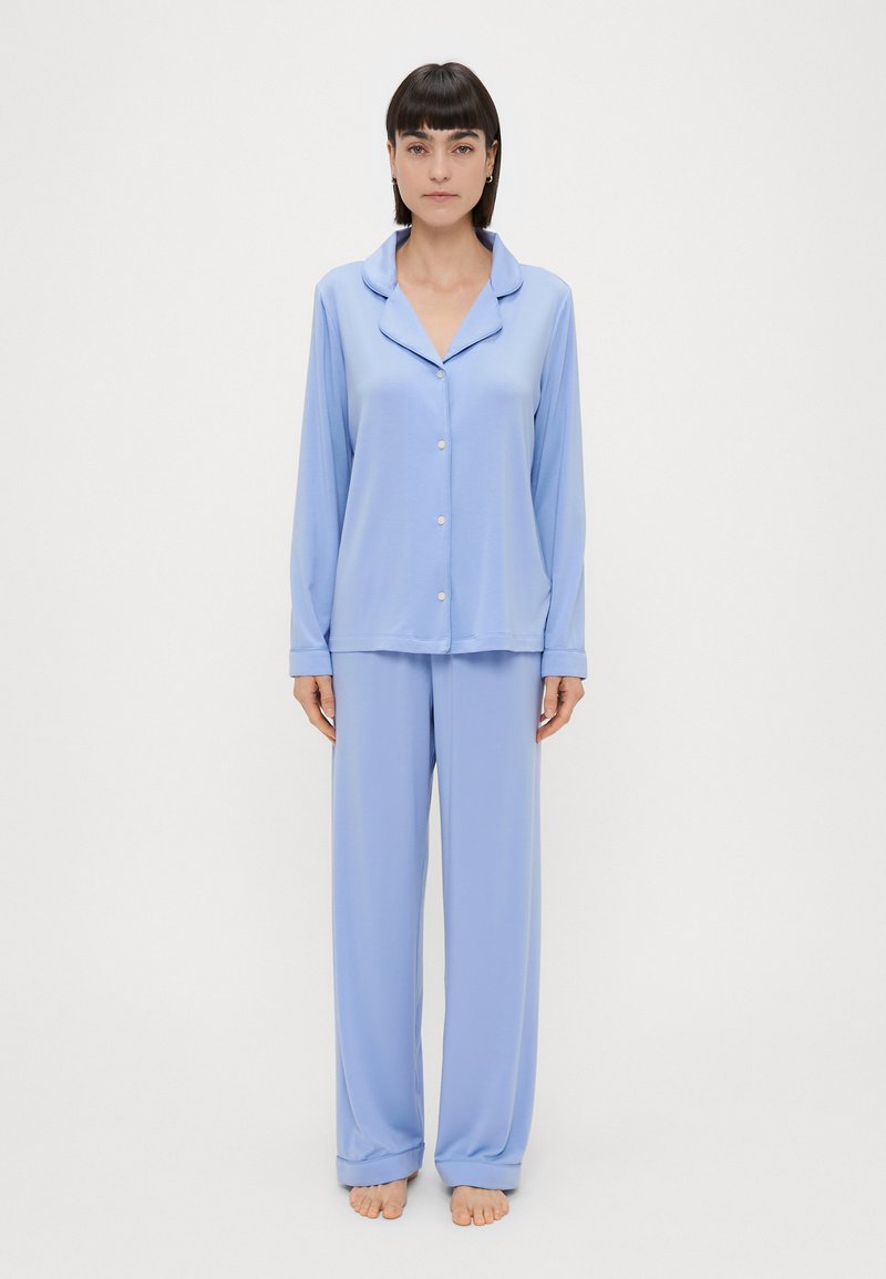 Conjunto de pijama de manga longa azul claro, feito de um tecido suave. Apresenta um colarinho, fecho de botões à frente e calças largas com bainhas ajustadas.