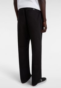 Black wide-leg pants made of a smooth fabric, featuring two back pockets and subtle branding near the waistband. Worn with black sneakers.