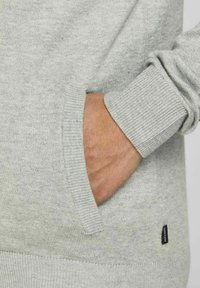 Šedý pulovr s žebrovanými manžetami a detaily kapes. Měkká pletenina s texturovaným vzhledem. Malá značka viditelná na boku.