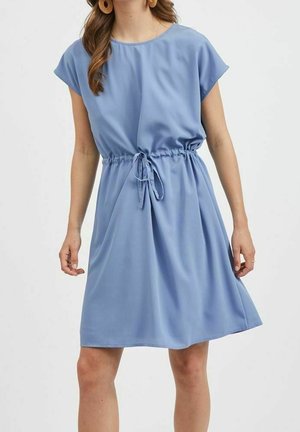 Nainen pukeutuneena vaaleansiniseen, lyhythihaiseen polvipituiseen mekkoon, jossa on sidottu vyötärö nauhalla.