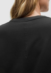 Sweatshirt noir avec un col rond côtelé, en coton doux, et un détail de couture à l'arrière. Texture simple et lisse.