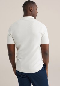 Poloshirt in licht crèmekleur, korte mouwen, gestructureerde stof met een subtiel patroon, getailleerd ontwerp, geribbelde kraag en zoom. Gecombineerd met marineblauwe broek.