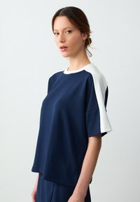 Marineblauw t-shirt met korte mouwen en witte schouderaccenten. Gemaakt van een gladde stof, met een casual pasvorm en een ronde halslijn.