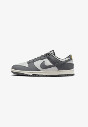 Niski sneaker Nike z szarej i białej skóry z czarną podeszwą i sznurowaniem, widoczny z boku na białym tle.