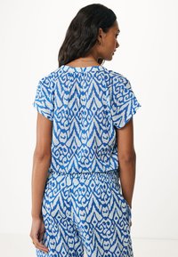 Top blu con motivo a fantasia, maniche corte, caratterizzato da un design ikat. Tessuto leggero, fitting comodo e dettaglio plissettato sul retro.