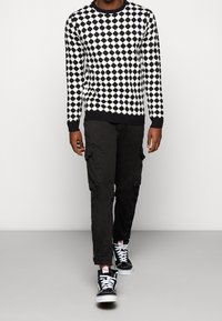 Černobílý svetr se vzorem diamantů, doplněný černými cargo kalhotami a černými kotníkovými teniskami s bílými detaily.