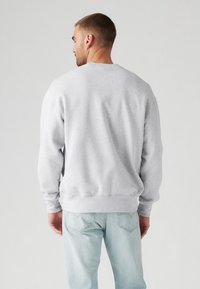 Gray sweatshirt made of cotton blend with a crew neck, ribbed cuffs, and waistband. Worn with light blue jeans, showing a minimalist design.